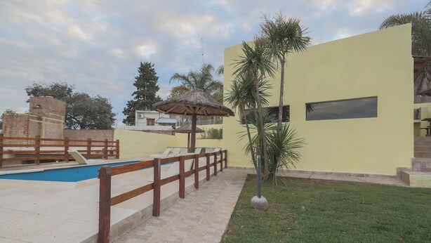 A swimming pool with a wooden fence, a thatched umbrella, and a palm tree.