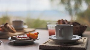 A breakfast setting with a cup, a plate with toast and fruit, and a bowl of bread on a wooden table.