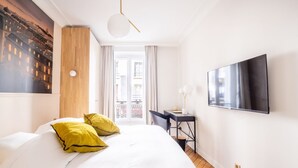 Une chambre d’hôtel avec un grand lit, un bureau, une télévision et une fenêtre donnant sur des immeubles.