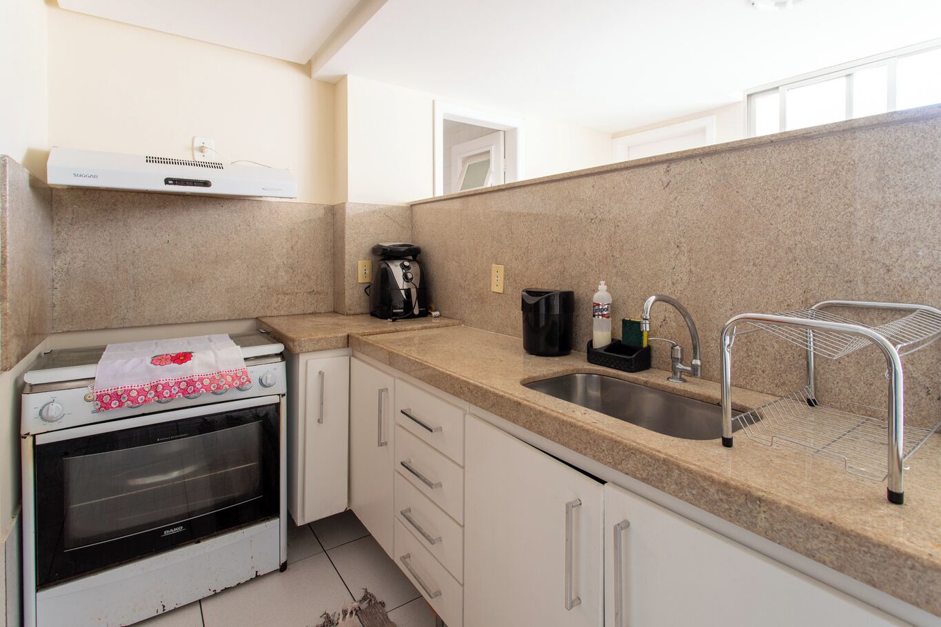 A compact kitchen with a built-in oven, a coffee maker, and a sink with a metal drying rack.