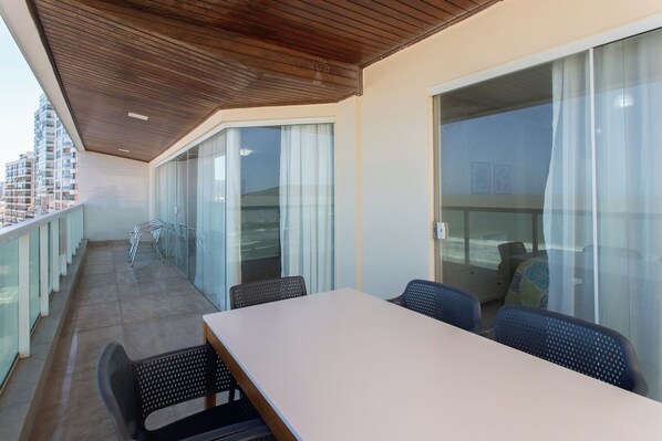A balcony with a table and chairs, glass doors, and a view of the city. - Apto Pet Friendly com 3 Su tes e Vista Para o Mar (Guarapari)