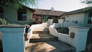 A house with a stone staircase leading to a front door, surrounded by a white wall and greenery. - The Sleepy Hollow Hideaway (Gold Canyon)