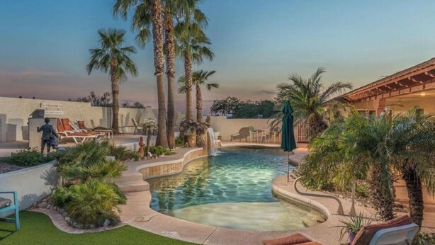 A pool area with palm trees, lounge chairs, and a waterfall feature. - The Sleepy Hollow Hideaway (Gold Canyon)