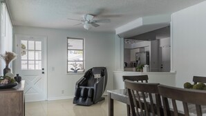A clean, modern kitchen with a built-in oven and microwave, a dining area with a table and chairs, and a massage chair in the corner.