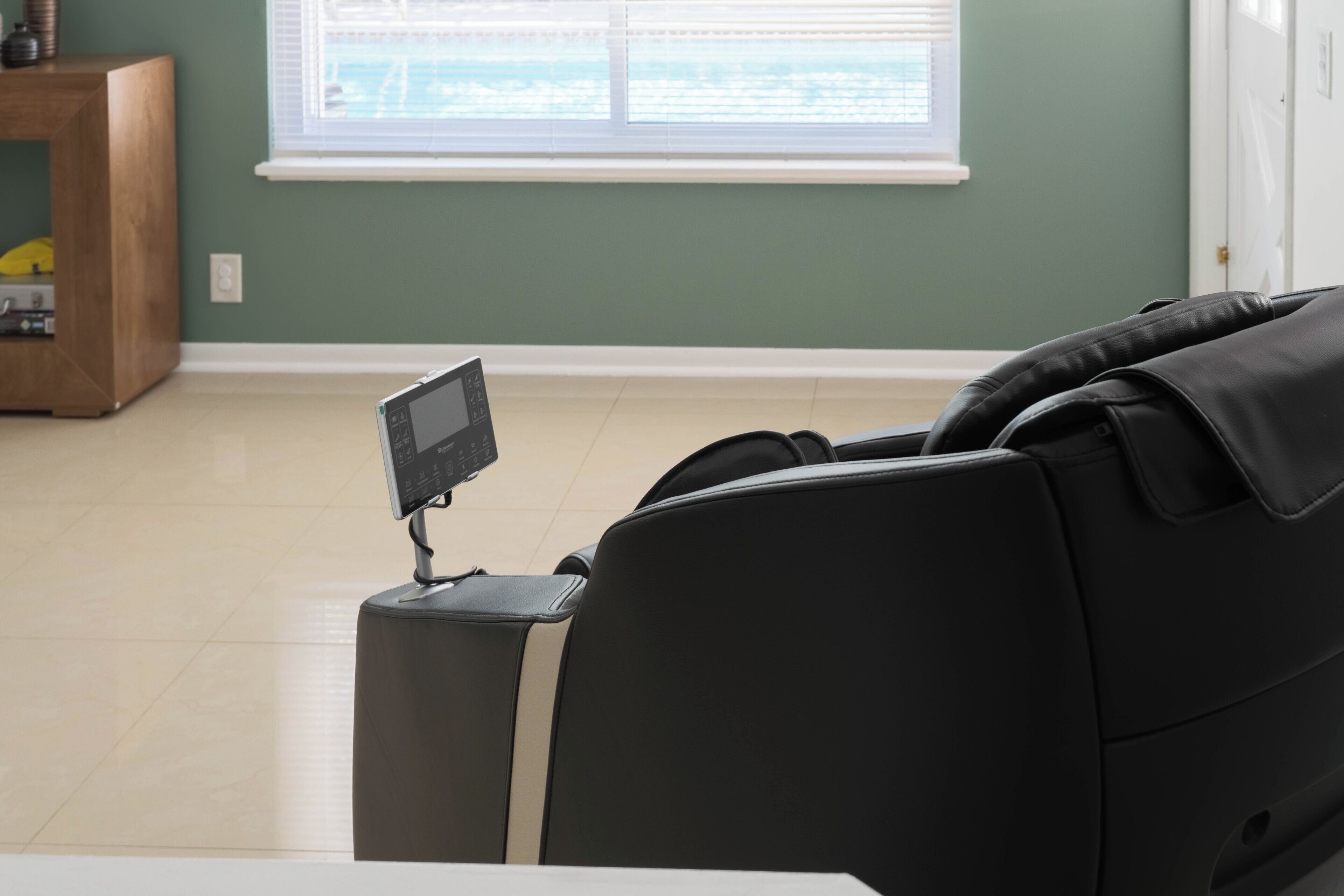 Uma cadeira de massagem com painel de controle, um armário de madeira e uma janela com persianas.