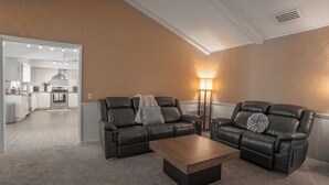 A modern living room with two leather sofas, a wooden coffee table, and a floor lamp. A kitchen is visible in the background.