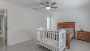 Una habitación amplia y bien iluminada con una cuna blanca, una cama de madera y una mesita de noche.