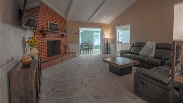 A living room with a brick fireplace, a sofa, a coffee table, and a dining area in the background.