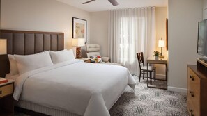Ein Hotelzimmer mit einem großen Bett, einem Schreibtisch, einem Sessel, einem Fernseher und einem Deckenventilator.