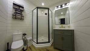 Ein Badezimmer mit Duschkabine, Toilette, Waschbecken mit goldenen Armaturen und einem Handtuchhalter mit Handtüchern.