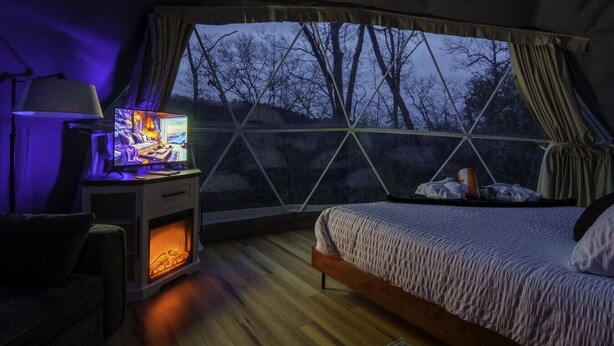Un dormitorio acogedor con una cama, un escritorio con una computadora y una ventana con vistas a árboles.