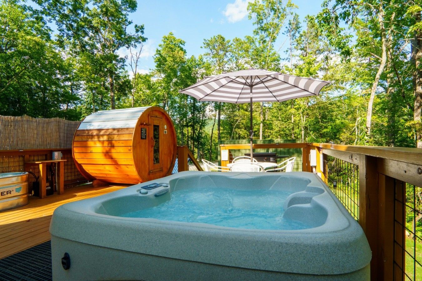 Un bain à remous sur une terrasse en bois, avec un sauna et un parasol.