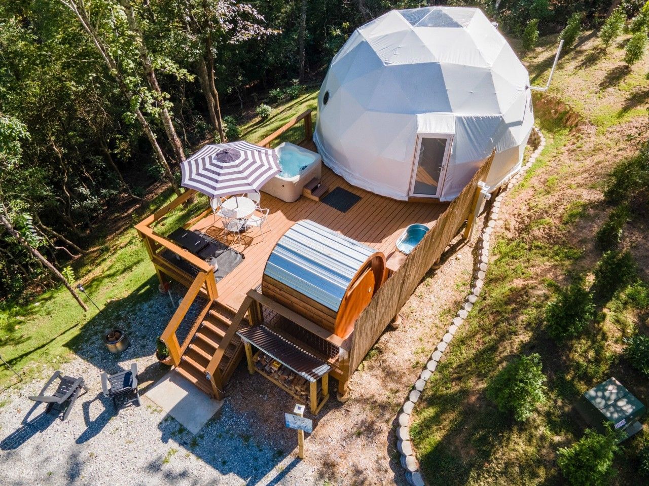 Une structure en forme de dôme géodésique dotée d’une terrasse, d’un espace salon extérieur et d’un coin barbecue.