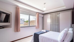 Une chambre d’hôtel avec un lit, un téléviseur fixé au mur, une fenêtre avec des rideaux et une armoire.