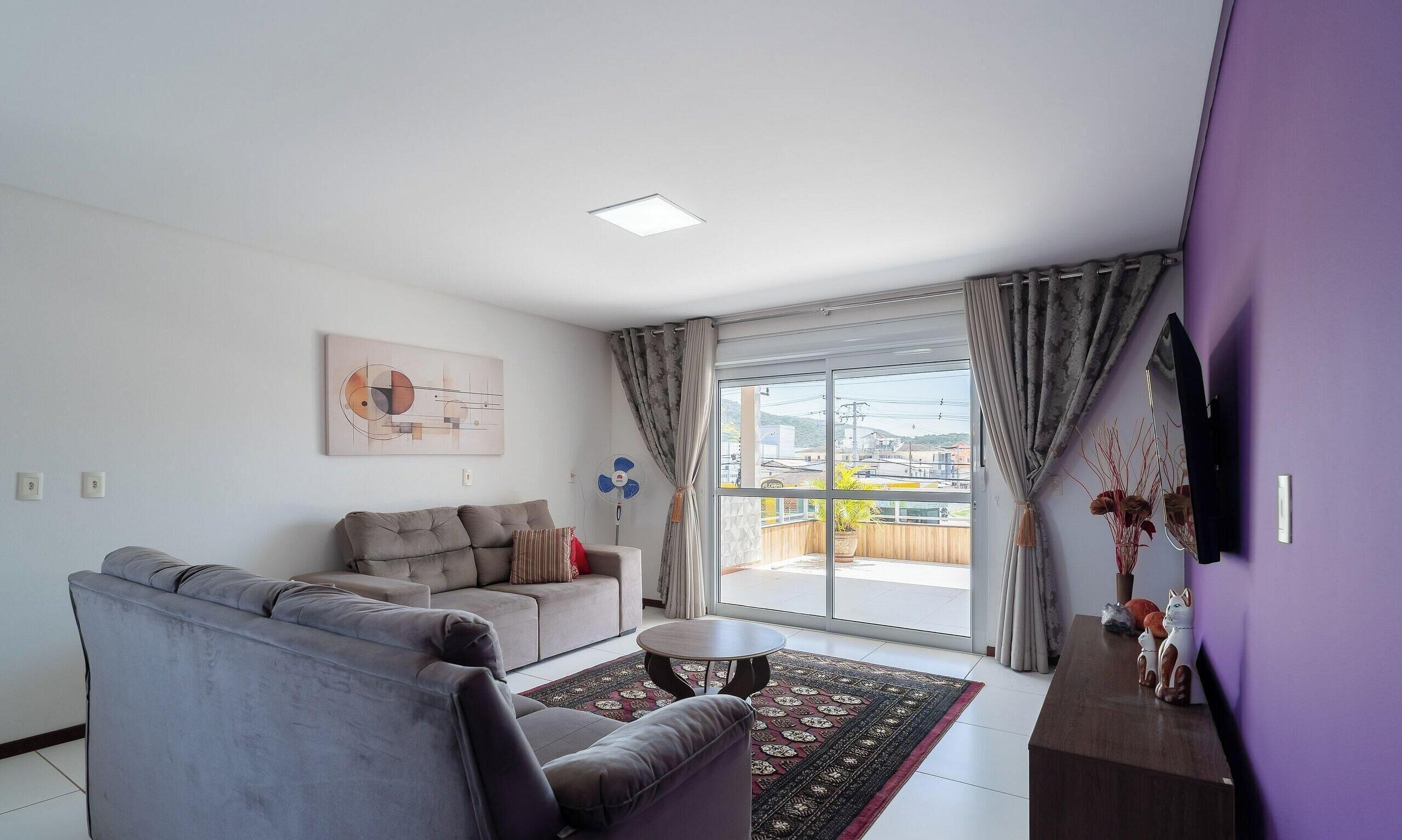 A modern living room with a grey sofa, a small round table, and a large window with curtains.