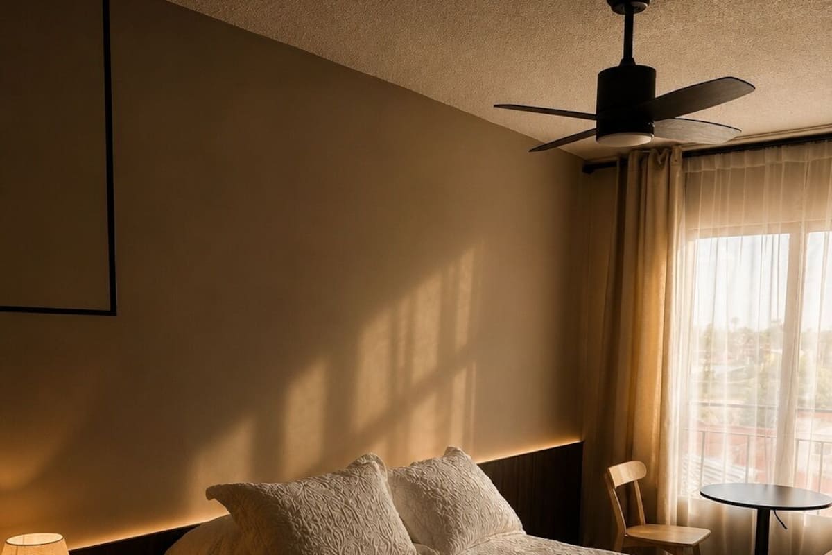 A hotel room with a bed, a desk, a chair, a ceiling fan, and a window with curtains.
