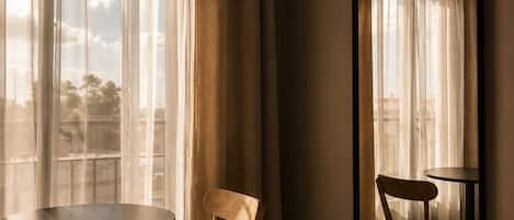 A hotel room with a bed, two chairs, a round table, a large mirror, and sheer curtains.