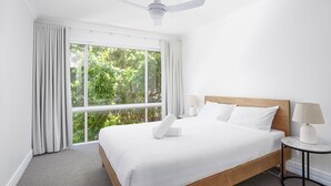 Hotelkamer met een groot bed, twee nachtkastjes met lampen, een plafondventilator en uitzicht op groen buiten het raam.