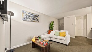 Un salon avec un canapé blanc, une table basse, un lampadaire et un tableau accroché au mur.