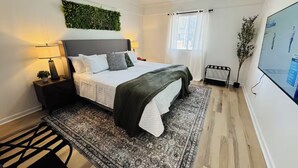 A modern bedroom with a bed, a ceiling fan, a wall-mounted green plant, a nightstand, a lamp, a window with curtains, and a TV on the wall. - Redbud: Waterfront, Augusta Canal, 3BR, king bed (Augusta)