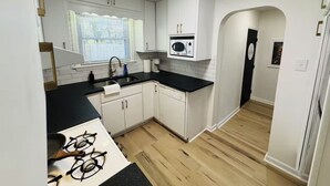 A modern kitchen with white cabinets, a black countertop, and a gas stove. - Redbud: Waterfront, Augusta Canal, 3BR, king bed (Augusta)