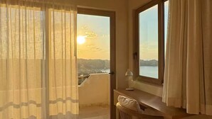 Ein Zimmer mit Blick auf einen Sonnenuntergang über einer Stadtlandschaft, einem Holztisch, einem Stuhl und einem großen Fenster mit Vorhängen.