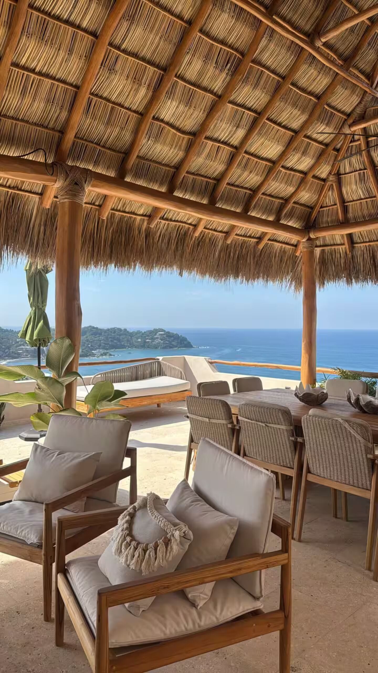 An outdoor seating area with thatched roof, wicker furniture, and a view of the sea.