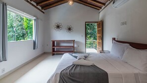 Quarto com cama grande, mesa de cabeceira de madeira, prateleira na parede e janela com cortinas.
