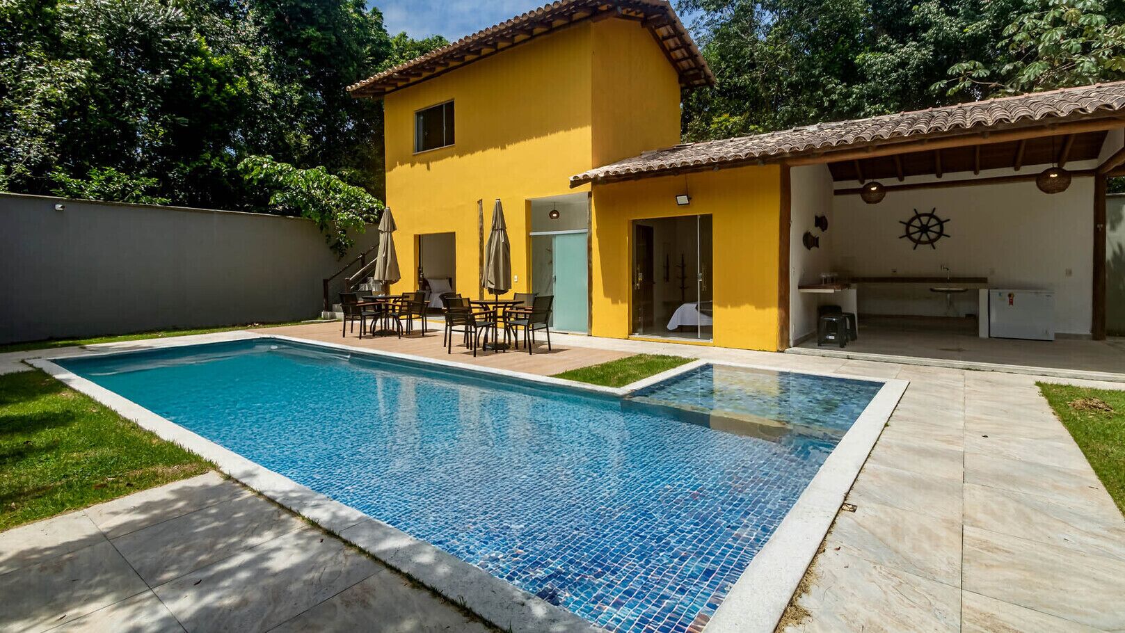 Une piscine dont les bords sont recouverts de carreaux, entourée d’un patio aménagé avec du mobilier d’extérieur.