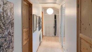 A hallway with wooden doors, framed artwork on the walls, and a hanging light fixture.