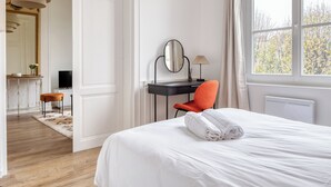 A hotel room with a large bed, a desk with a chair, a television, and a window with curtains. - Le Lauroise, magnifique F2 place des Carmes (Rouen)