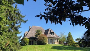 Une maison avec un toit en pente, entourée d’une pelouse verdoyante et d’arbres.