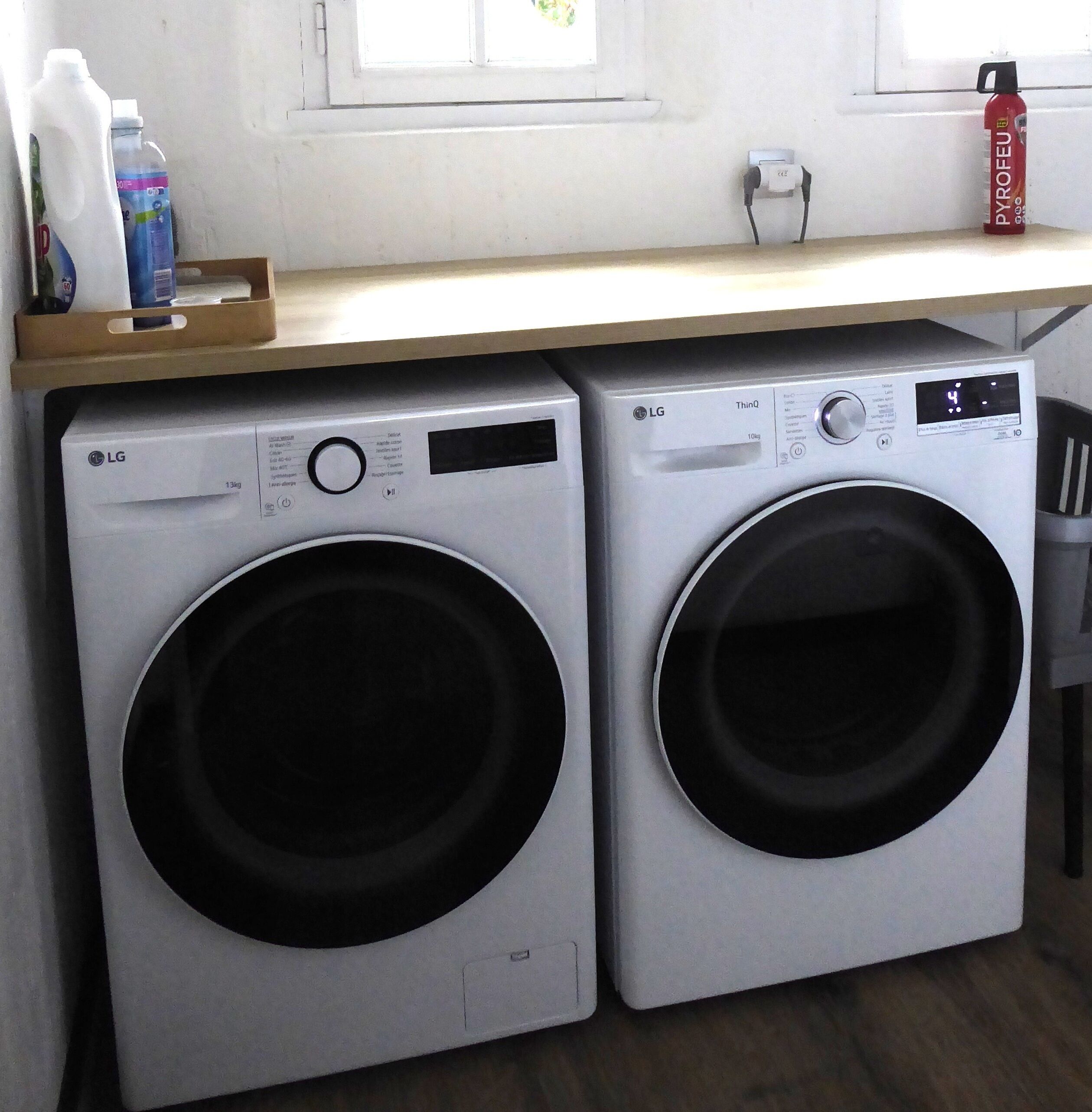 Two LG ThinQ front-loading washing machines in a laundry room with a wooden shelf above containing cleaning supplies.