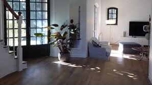 Un salon spacieux avec un escalier, une grande fenêtre, un canapé, un téléviseur et une plante.