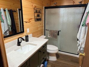 Un baño con detalles de madera, un lavabo blanco, un inodoro y un box de ducha de vidrio.