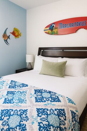 A hotel room with a bed, a pillow, a nightstand with a lamp, and a wall decoration. - Surf Studio • Steps to Beach • A/C • FREE Bikes (San Diego)