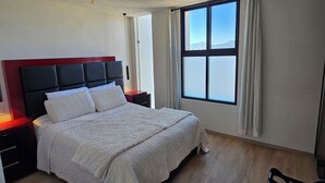Un dormitorio con una cama grande, una mesita de noche, una silla y una ventana con cortinas.