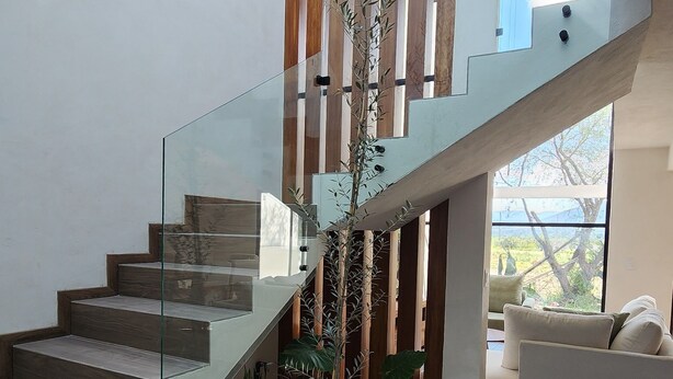 Una escalera moderna con barandillas de vidrio, una planta en maceta y un sofá blanco en un espacio de estar contemporáneo.