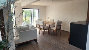 Una sala moderna con un sofá, una mesa de comedor y sillas. Hay un ventanal grande que proporciona luz natural y vistas al exterior.