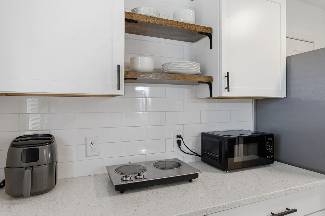 A kitchen with white cabinets, a toaster, a microwave, and a portable induction cooktop.
