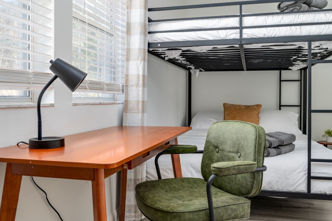 Ein Stockbett mit Schreibtisch und Stuhl, einer Lampe und einem Fenster mit Jalousien.
