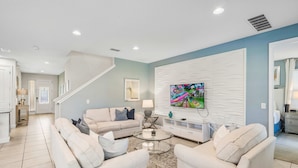 A modern living room with a sofa set, a coffee table, and a flat-screen TV mounted on a textured wall. - New 8BR Luxury Retreat • Pool & Spa • Near Disney (Kissimmee)
