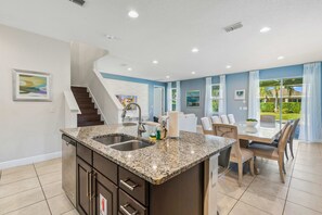 Una cocina moderna con encimeras de granito, lavavajillas integrado y comedor con mesa y sillas de vidrio.