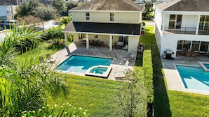 A residential property with a swimming pool, a covered patio, and a well-maintained lawn. - New 8BR Luxury Retreat • Pool & Spa • Near Disney (Kissimmee)