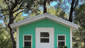 A small, single-story shed with a white door and two windows, surrounded by trees. - Fabulous private RV pad with full hookups, sewer and water located in Old Town (Old Town)