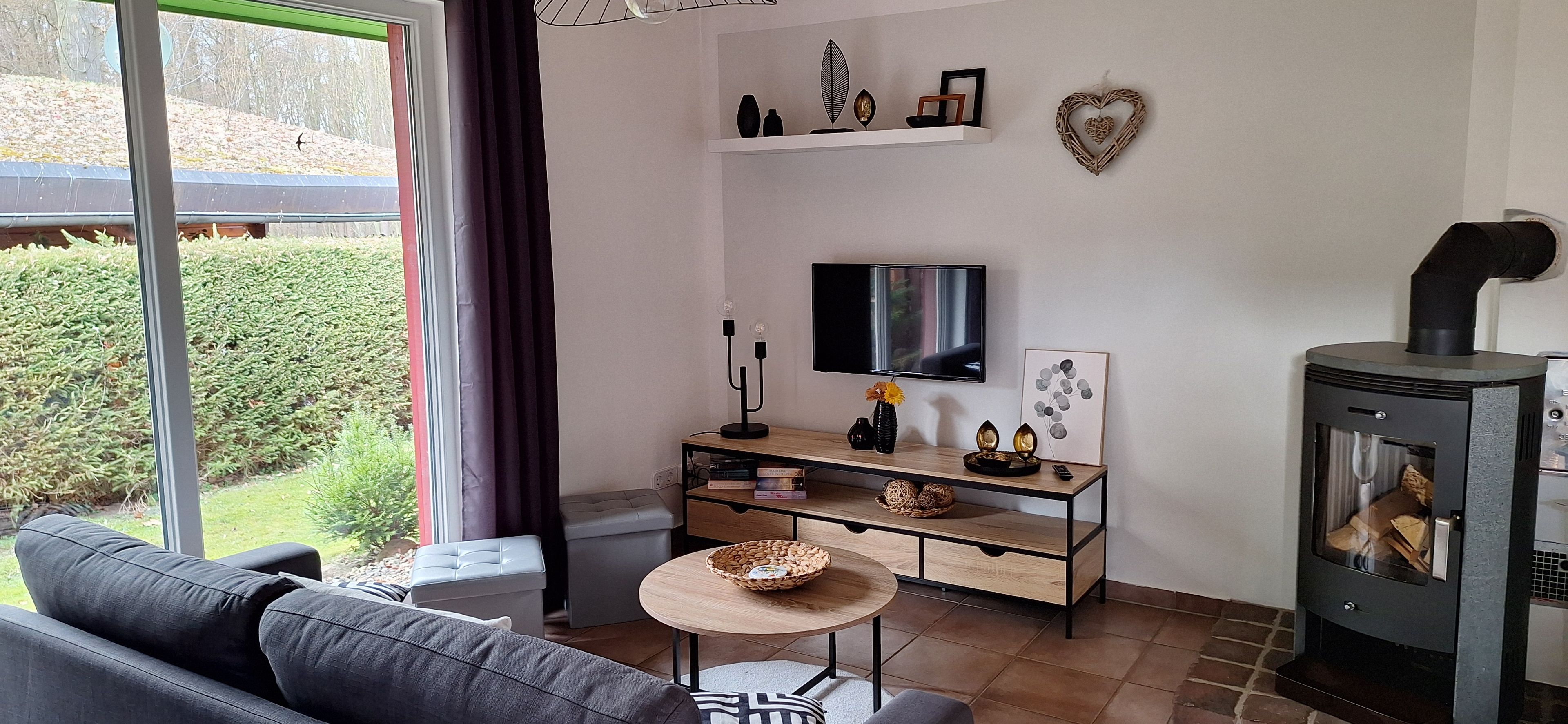 Ein Wohnzimmer mit einer Couch, einem Fernseher, einem Kamin und Blick ins Freie.