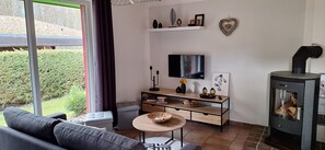 Una sala de estar con sofá, televisión, chimenea y vistas al exterior.