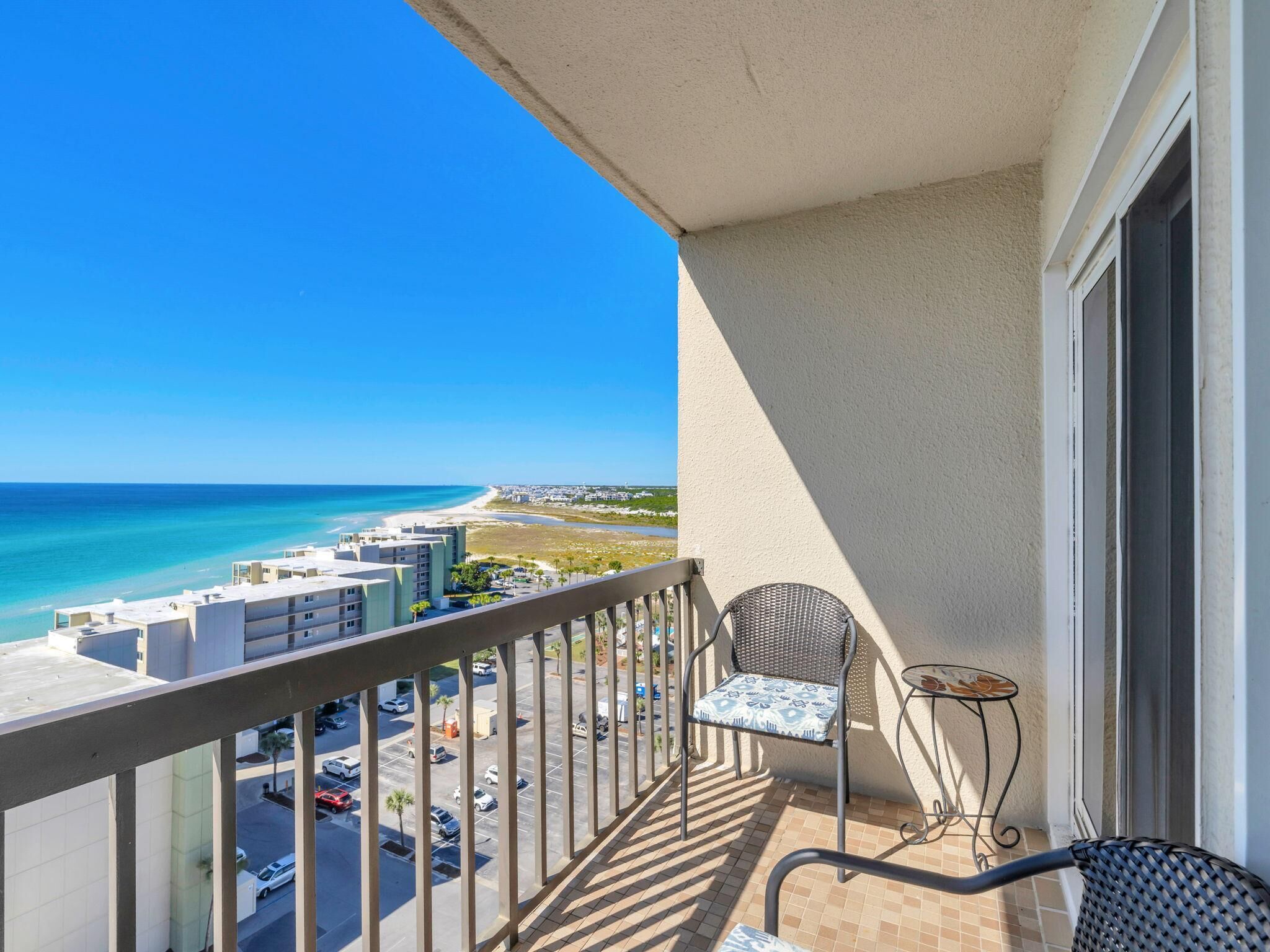 A balcony with a view of the beach, a chair, and a small table.