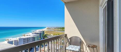 A balcony with a view of the beach, a chair, and a small table.