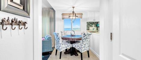 Un coin repas comprenant une table et des chaises, un lustre et une vue sur la mer par une fenêtre.